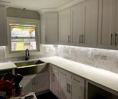 White kitchen cabinets with countertop and window; stainless steel sink.
