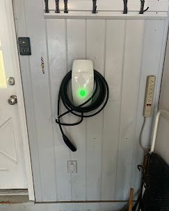 White electric car charger on a white wall, green light illuminated, cable coiled.