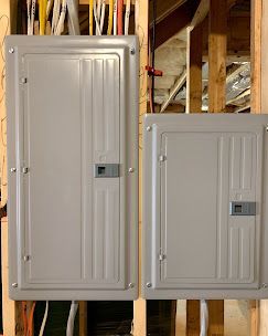 Two gray electrical panels mounted on wooden studs; wires visible.