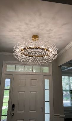 Gold chandelier with numerous white lights hanging above a white front door.