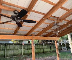 Covered outdoor patio with ceiling fan, chandelier, wood beams, and metal roof.
