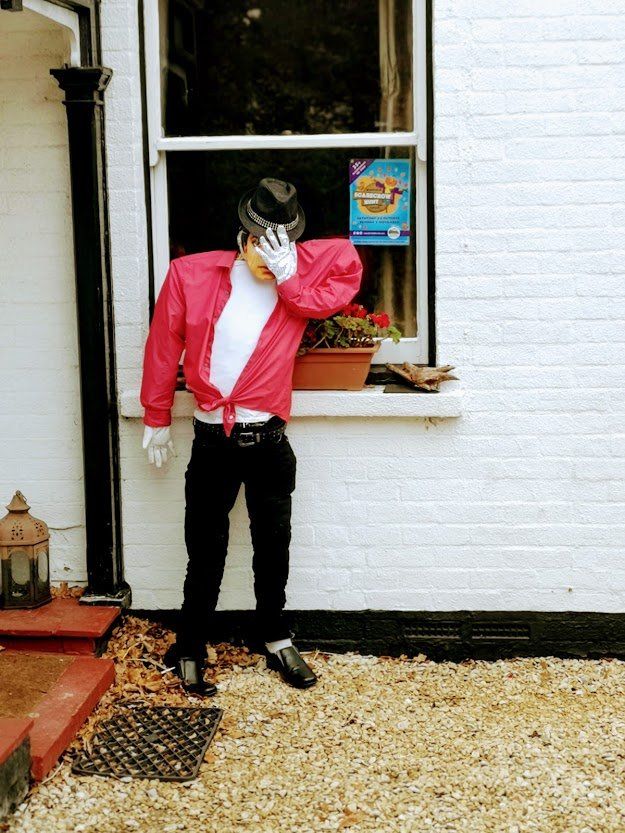 Mannequin dressed as Michael Jackson, wearing a red jacket and black pants, stands outside a white building.