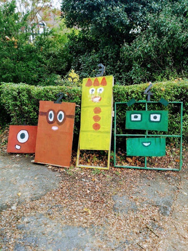 Four Numberblocks characters made of cardboard in a park setting.