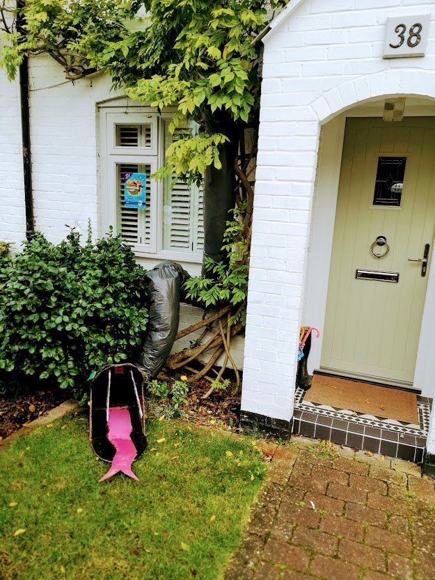 A house with a green door and a backpack on the lawn. A black trash bag is next to a window.