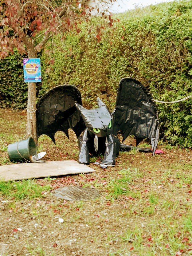 Toothless dragon sculpture made of black materials on a grassy area, with wings outstretched.