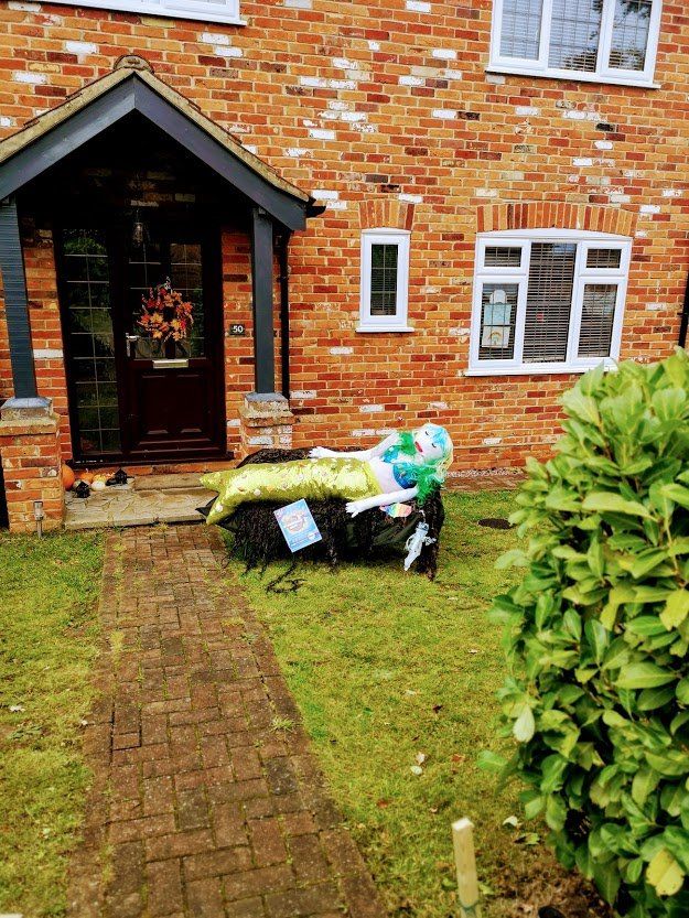 Brick house with a mermaid scarecrow on the front lawn. The mermaid has green hair and a yellow tail.