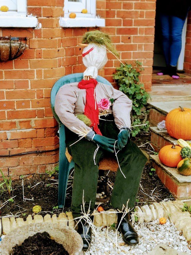 A scarecrow wearing a red tie and sitting in a chair, with pumpkins nearby.