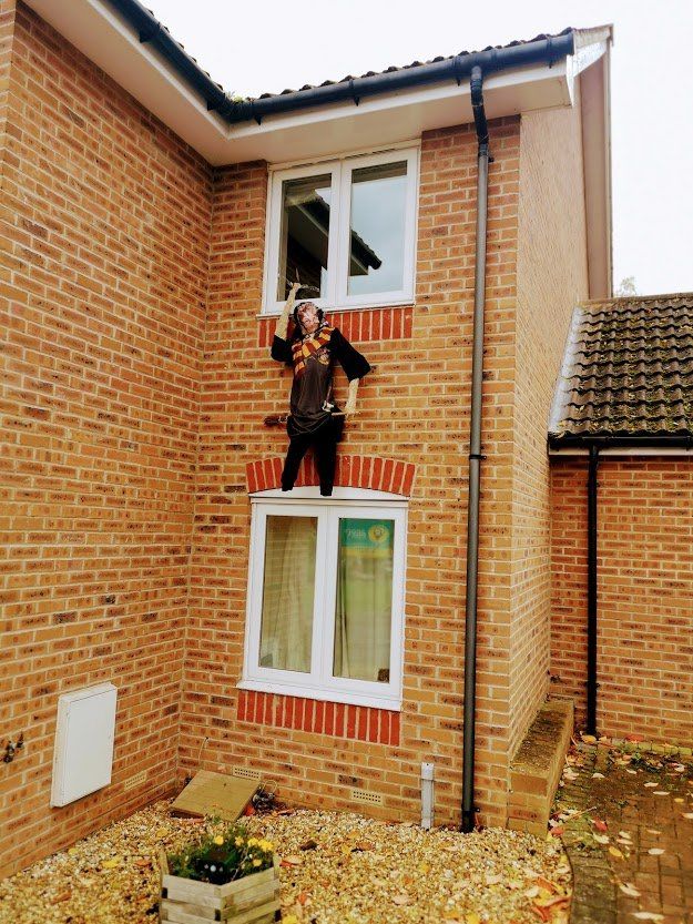 Person dressed in costume standing on a window ledge of a brick building.