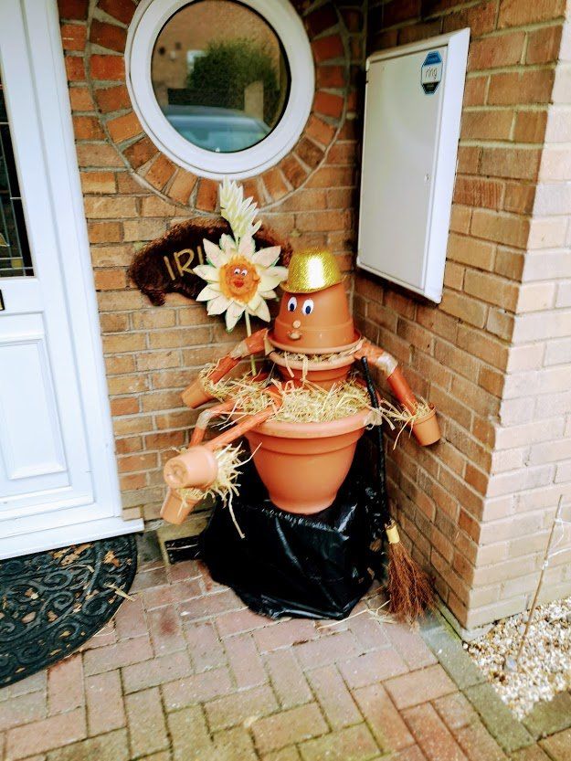 A scarecrow made of terracotta pots, straw, and a golden hat, standing by a door.