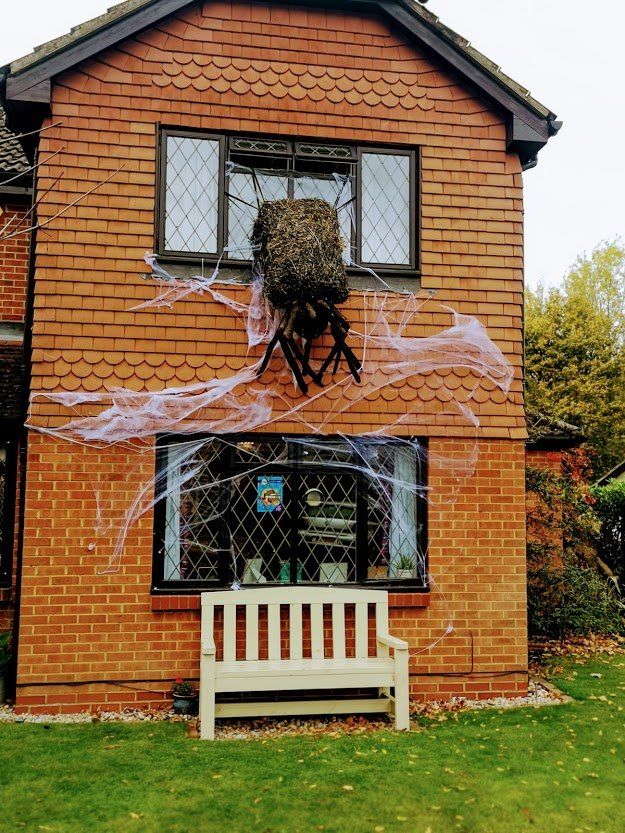 Brick house decorated for Halloween with a large spider, web, and a bench.