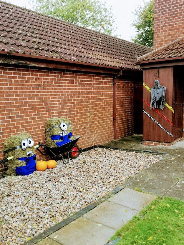 Two hay bale Minion characters and one Halloween decoration next to a brick building.