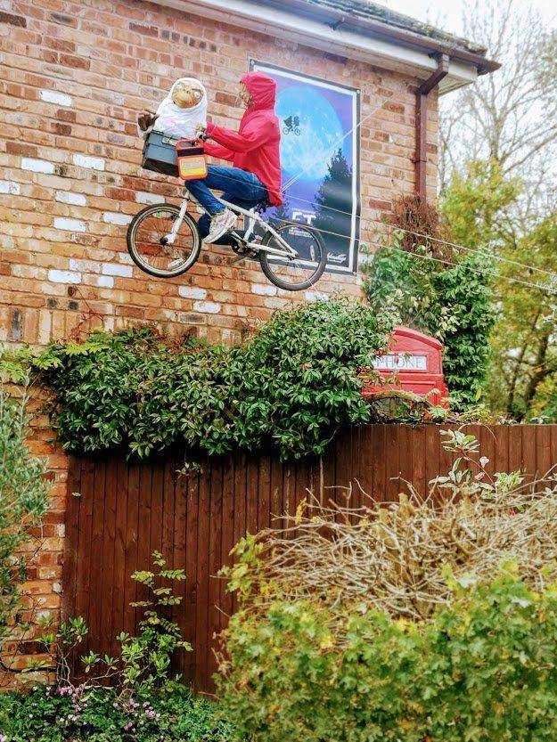 A bicycle sculpture with rider and alien, mounted on a brick wall, alongside an 