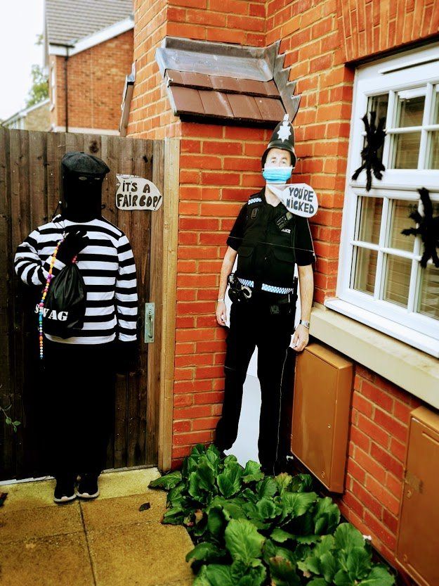 Cardboard cutout of a burglar and a police officer guarding a doorway next to a brick house.