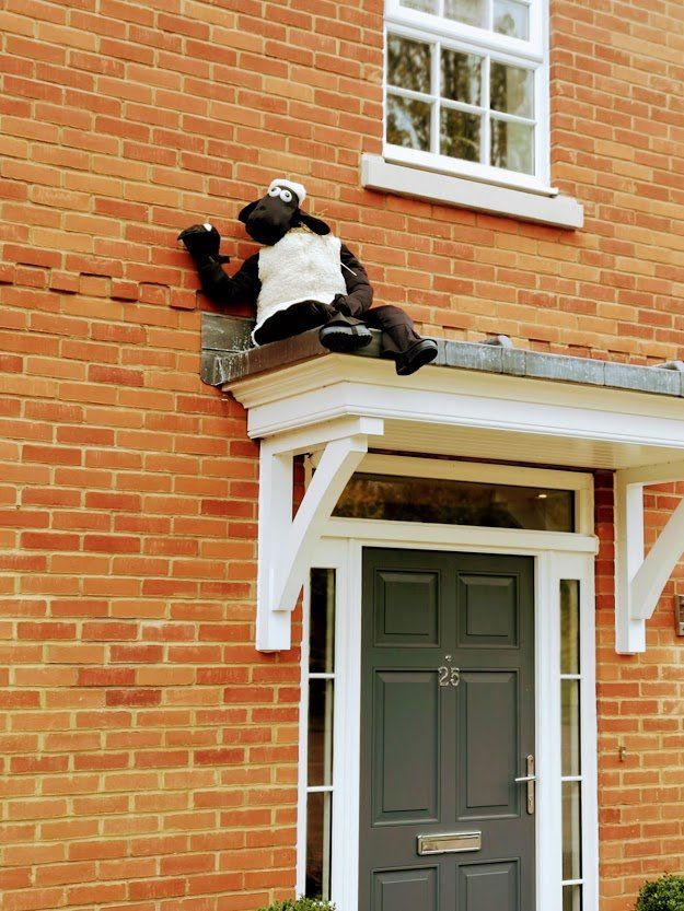Shaun the Sheep figure sitting on a porch roof, above a gray door on a brick building.