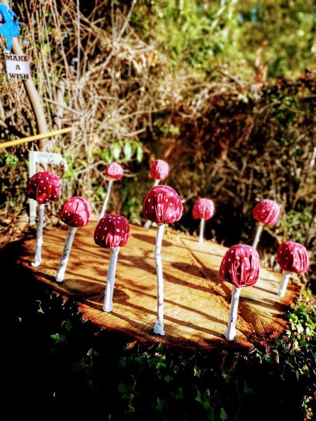 Red-capped mushroom sculptures on a tree stump in a garden setting.