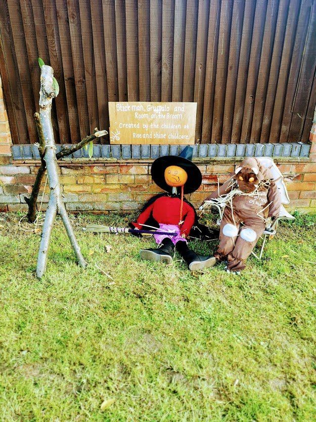 Three scarecrows on grass; a seated figure with hat and sunglasses next to another tied to a chair; a sign reads: 