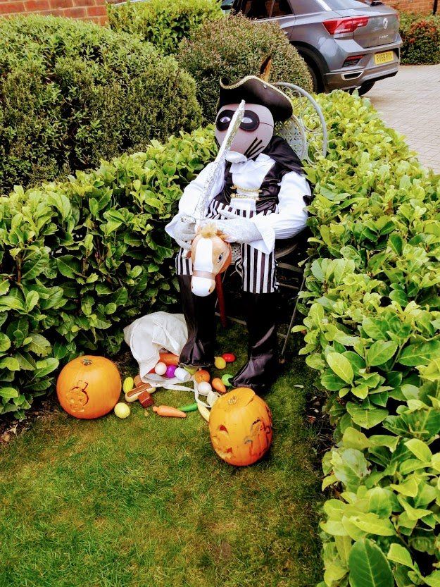A scarecrow dressed as a pirate with pumpkins and eggs on the grass.