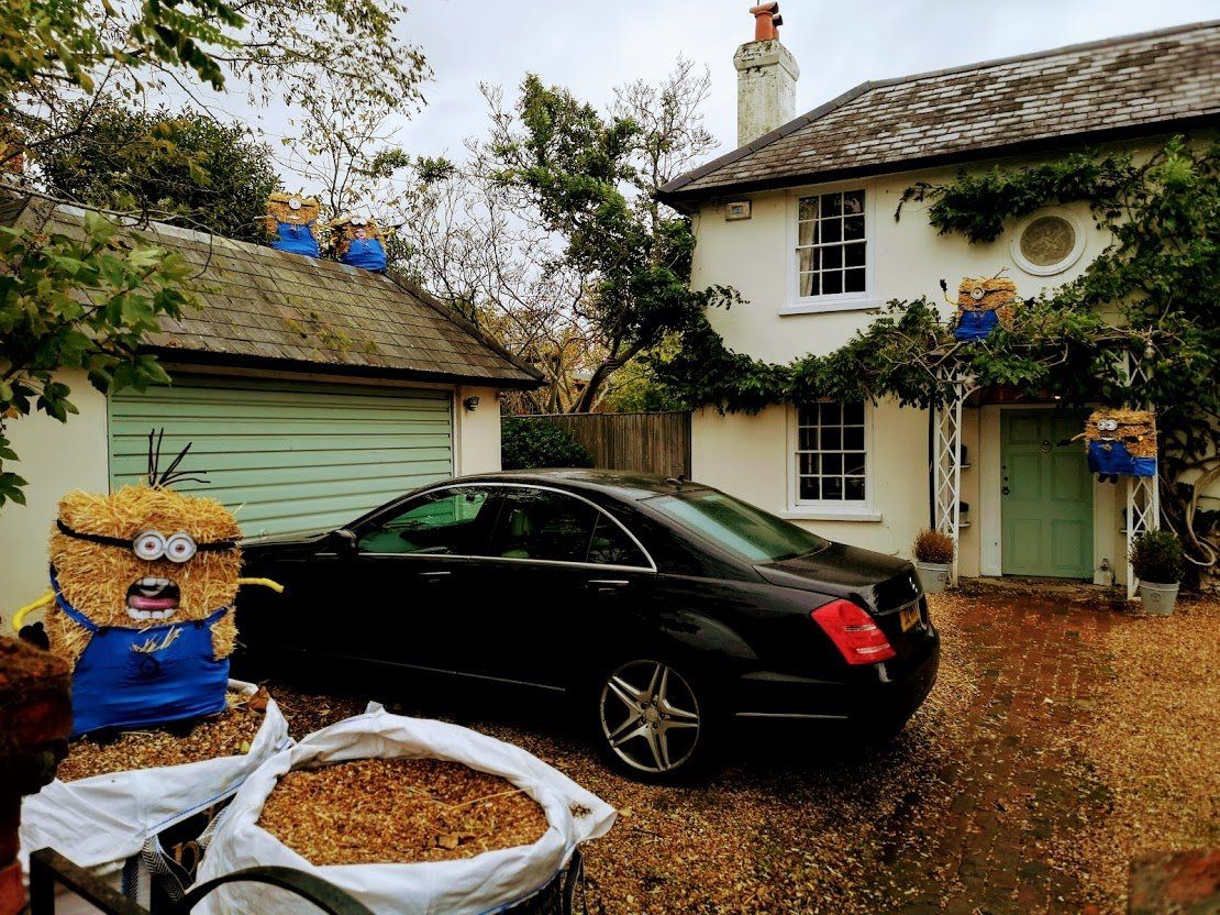 Black car parked in front of a white house with a garage and hay bale Minion decorations.
