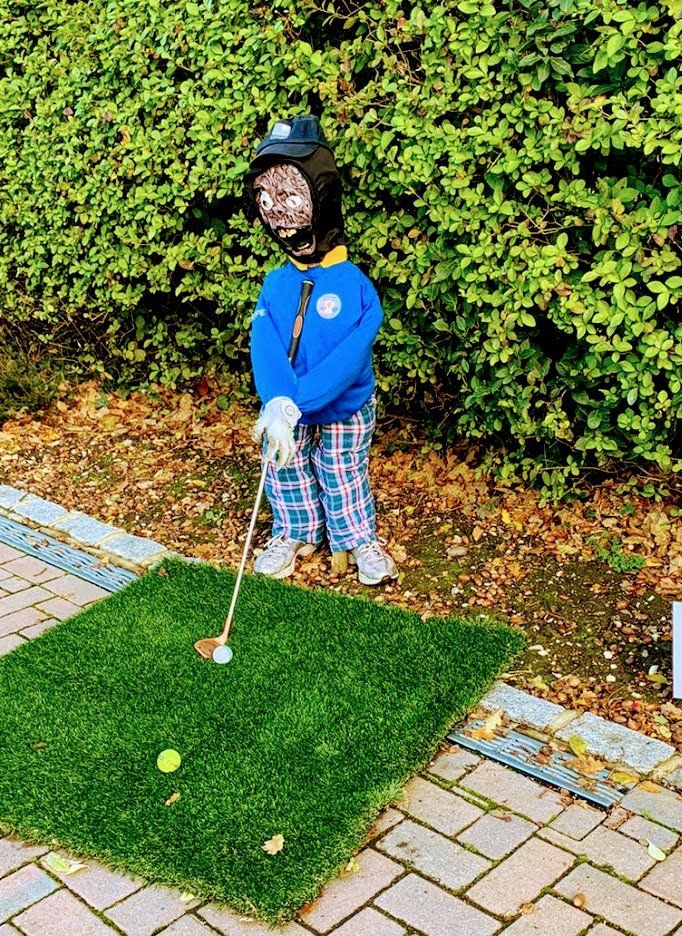 Scarecrow wearing golf attire poised to putt on a miniature green.