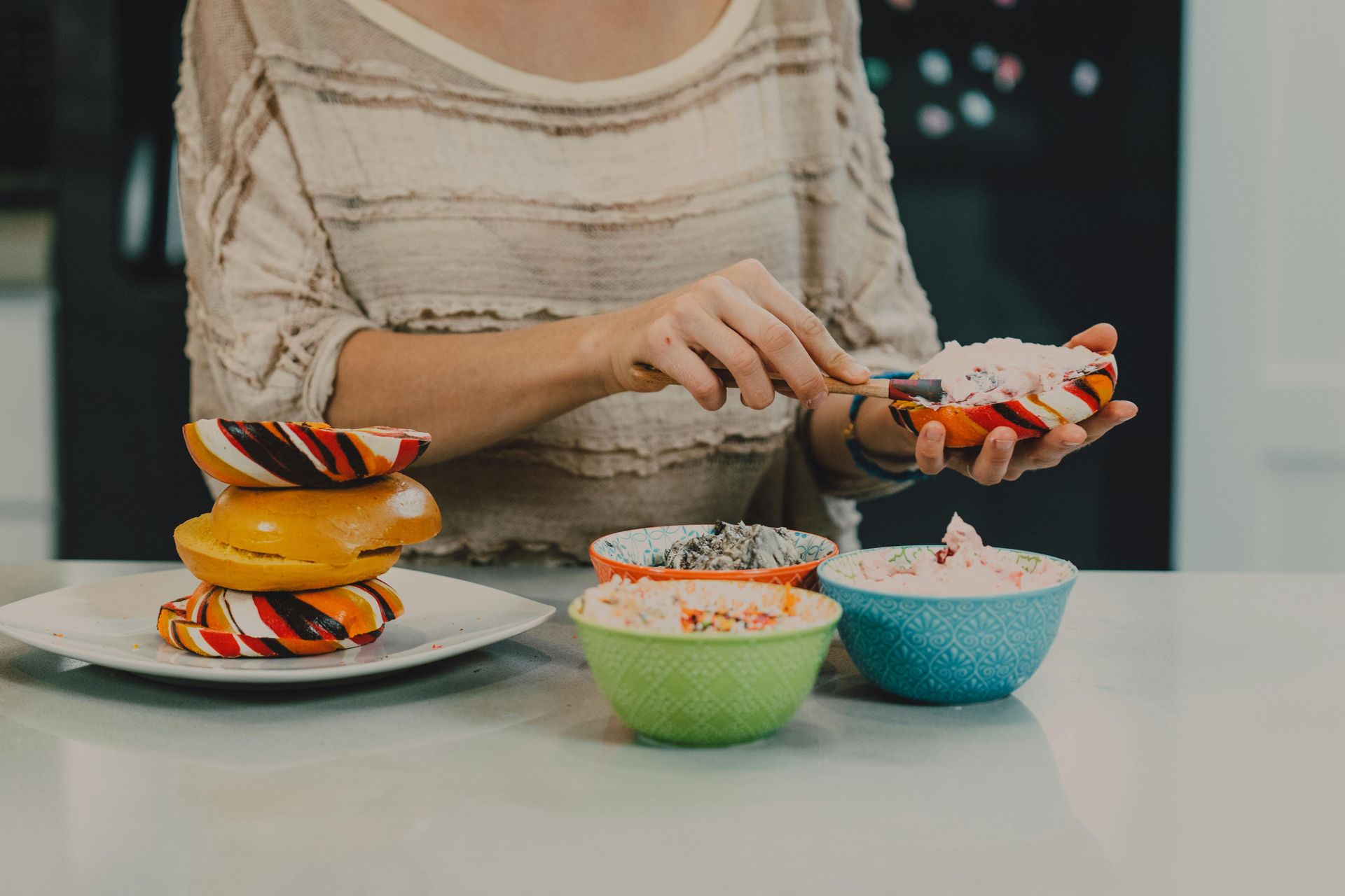 Woman decorating donuts with colorful sprinkles in a kitchen.