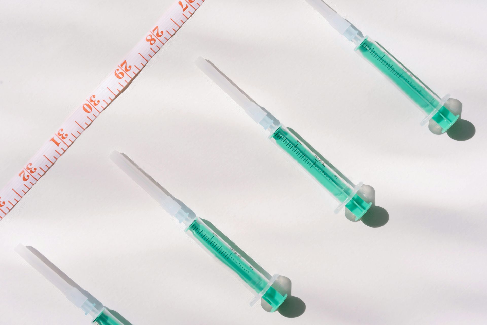 Four syringes are lined up next to a measuring tape.