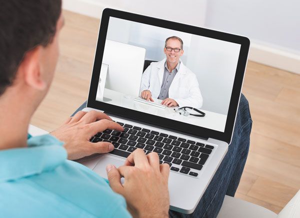 A man is sitting in front of a laptop computer talking to a doctor.