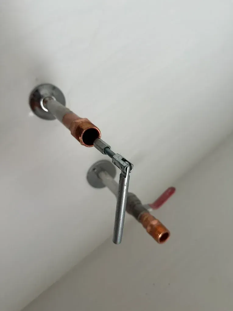 A close-up view of two exposed copper plumbing pipes protruding from a wall, with a small metal tool connected to one.