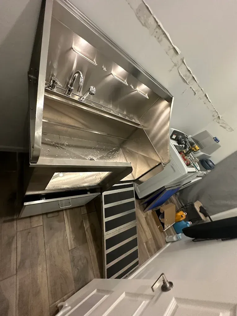 A stainless steel grooming tub with an attached ramp sits on a wood-look floor in a room with a white door and ceiling.