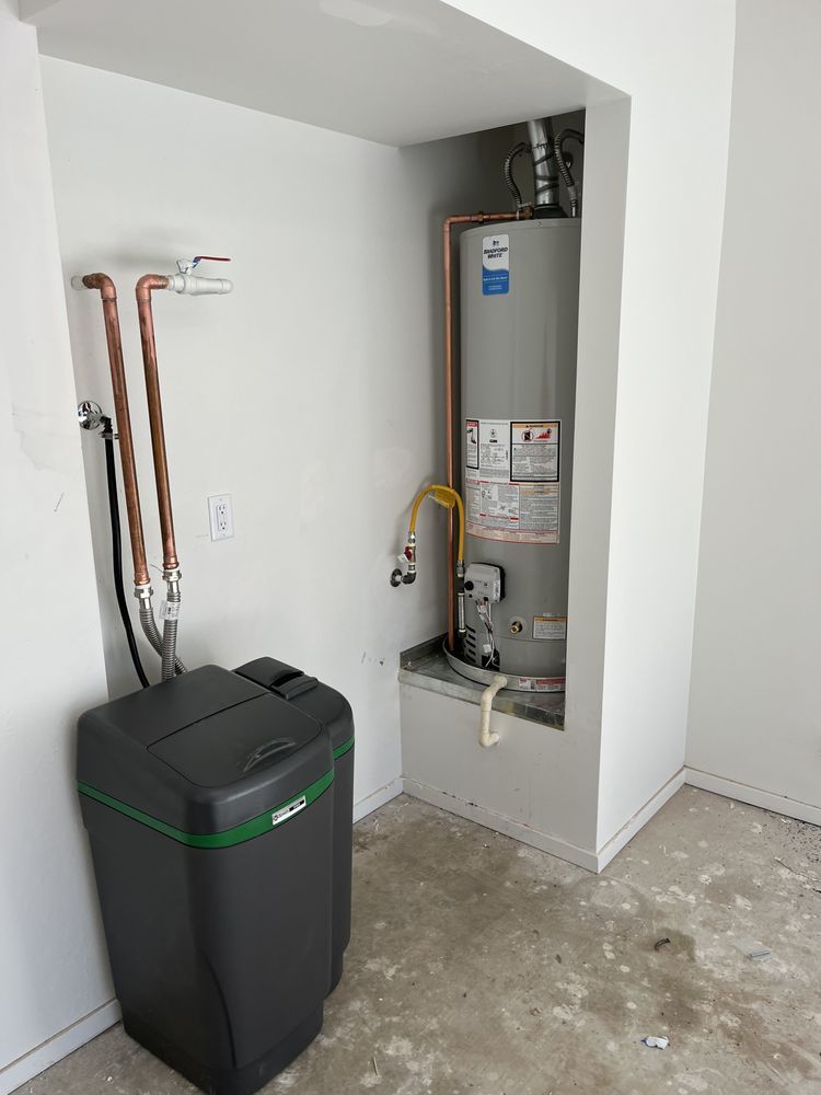 A grey water heater and a black water softener in a residential utility nook with copper plumbing connections.