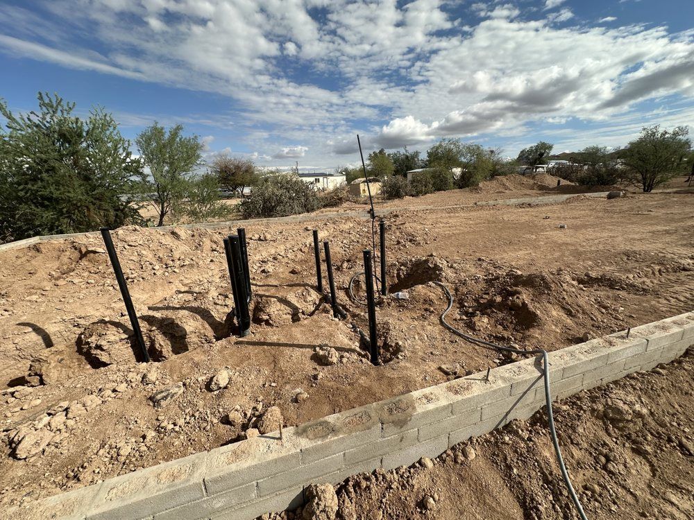A construction site showing vertical black pipes protruding from excavated dirt near a concrete foundation border.
