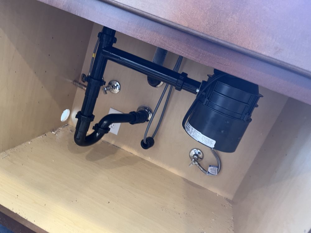 Under-sink cabinet view showing a black garbage disposal connected to plumbing pipes and water supply valves.