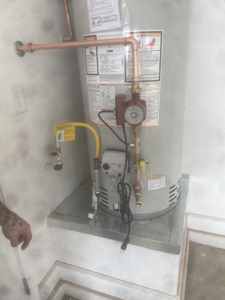 A water heater in a garage with a red recirculation pump installed on the copper piping.