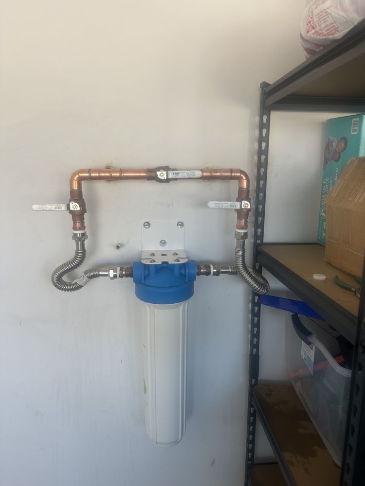 A water filtration system mounted on a wall with a copper pipe bypass loop and two control valves.