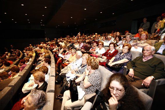 Público sentado en un teatro oscuro. Muchas personas mayores observan una función.