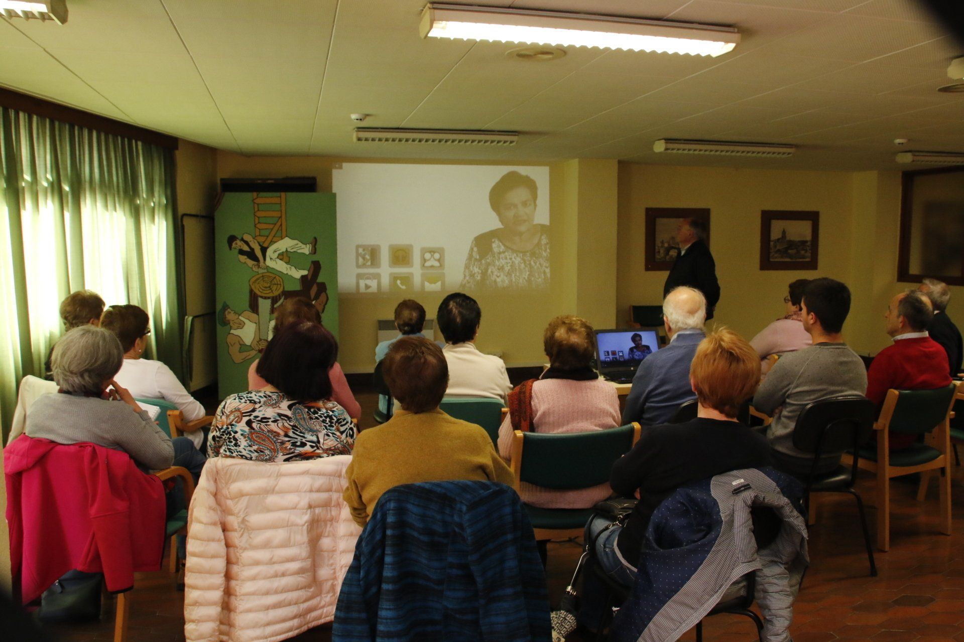 Un grupo mira una presentación en una sala con una pantalla, posiblemente una conferencia o un evento.