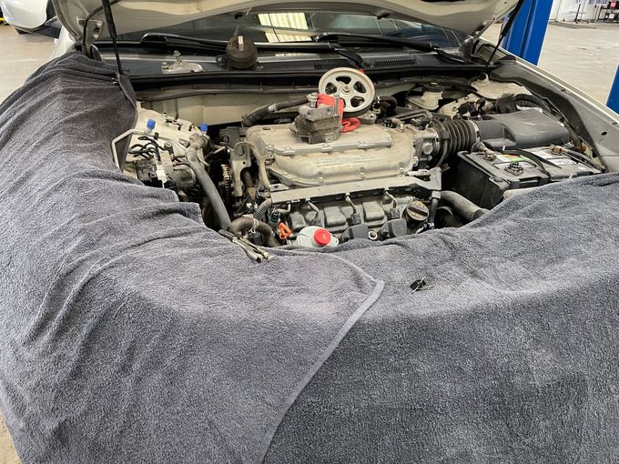 Car engine bay with hood open, showing a mechanic’s engine and covered fenders in a garage.| George Witt Service, Inc.