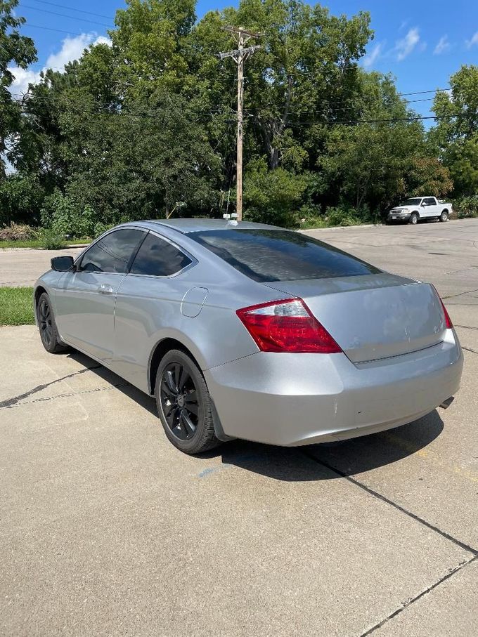 Silver two-door coupe parked on a concrete lot with trees in the background.| 