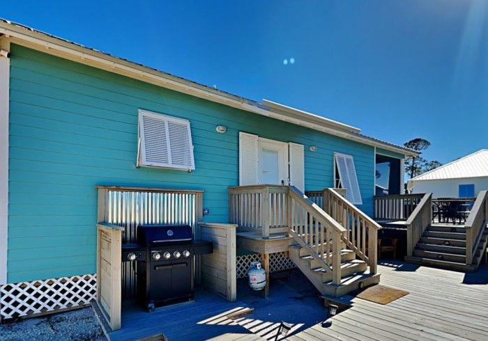 A blue house with stairs and a grill on the deck.