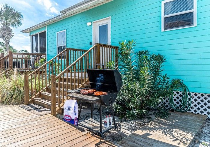 A blue house with a bbq grill on the deck.