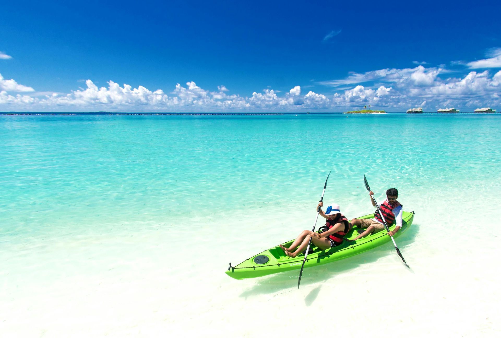 A man and a woman are sitting in a green kayak in the ocean.