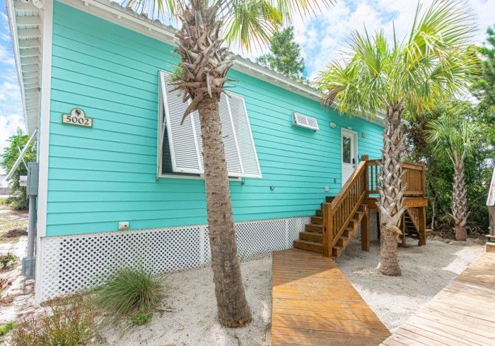 A blue house with palm trees in front of it and stairs leading up to it.