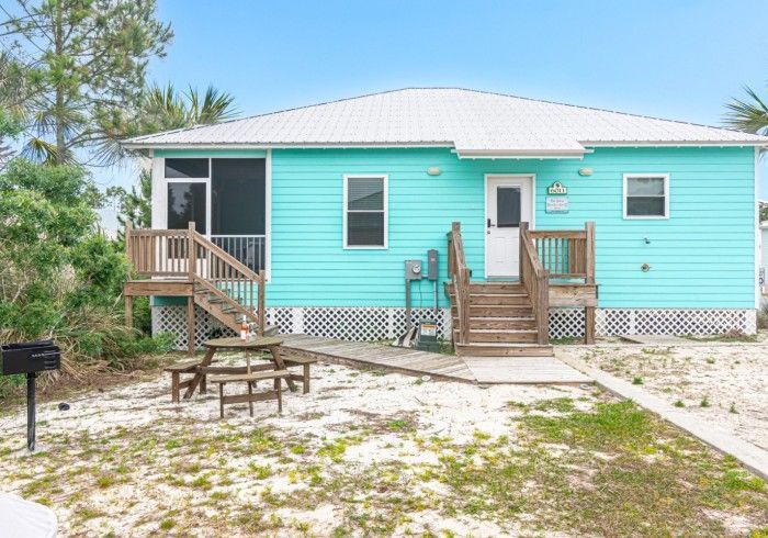 A blue house with a screened in porch and a picnic table in front of it.