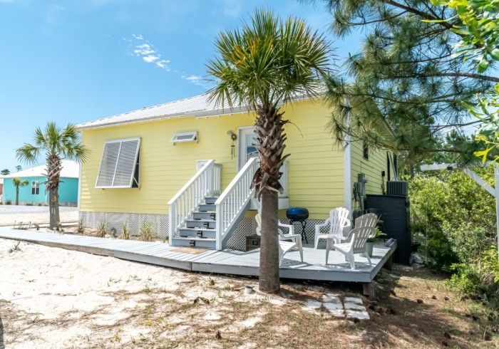 A small yellow house with stairs leading up to the second floor and a deck.
