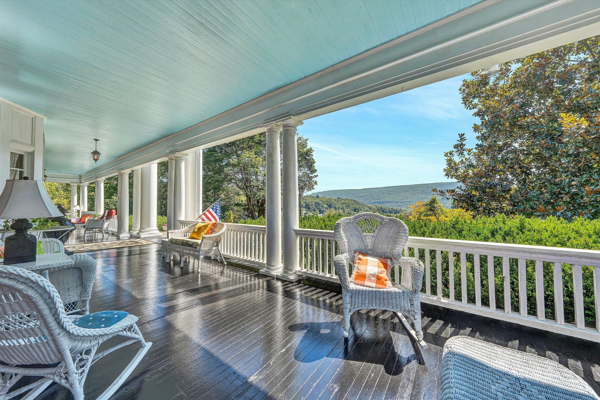 Covered porch with white columns, chairs, and a scenic view of trees and hills