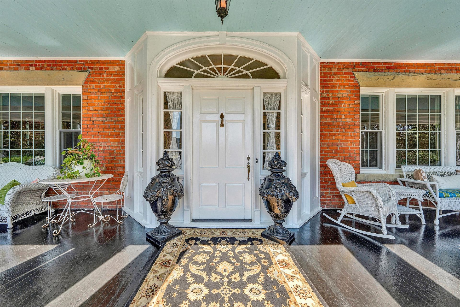 Front porch with white double doors, red brick walls, and patterned outdoor rug between white seating areas