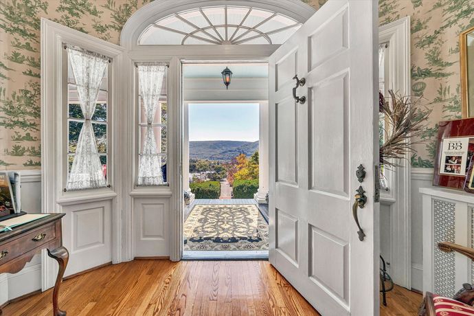 Open front door to a bright foyer with bay windows, hardwood floors, and a view outside