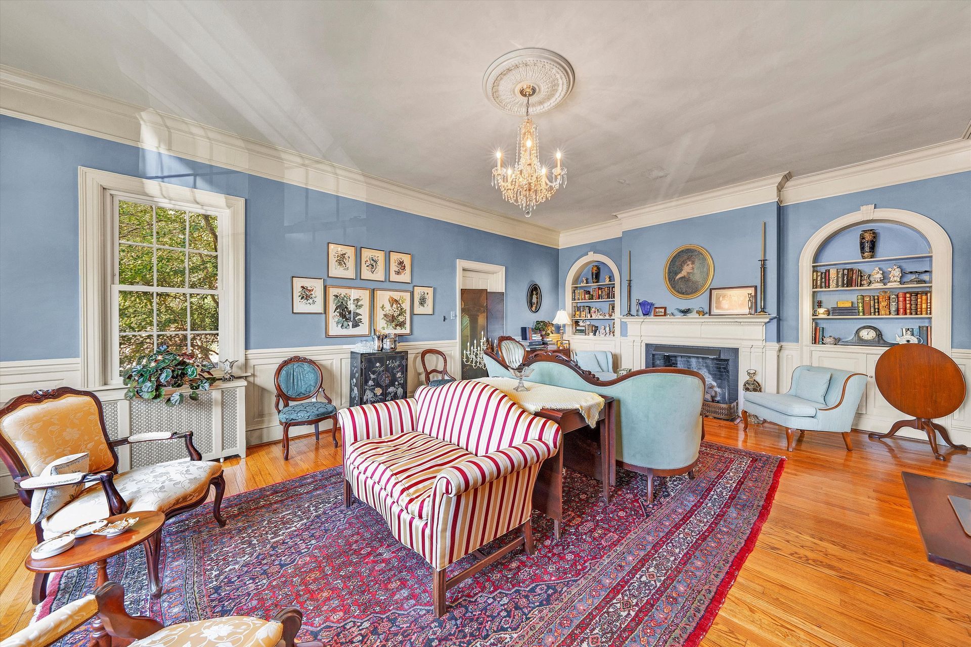 Bright blue living room with striped chairs, red rug, arched shelves, and a chandelier