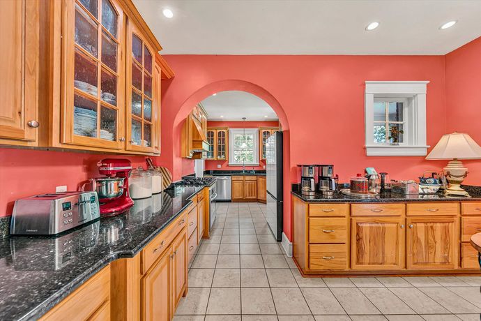 Bright kitchen with coral walls, wood cabinets, black countertops, and tiled floor.