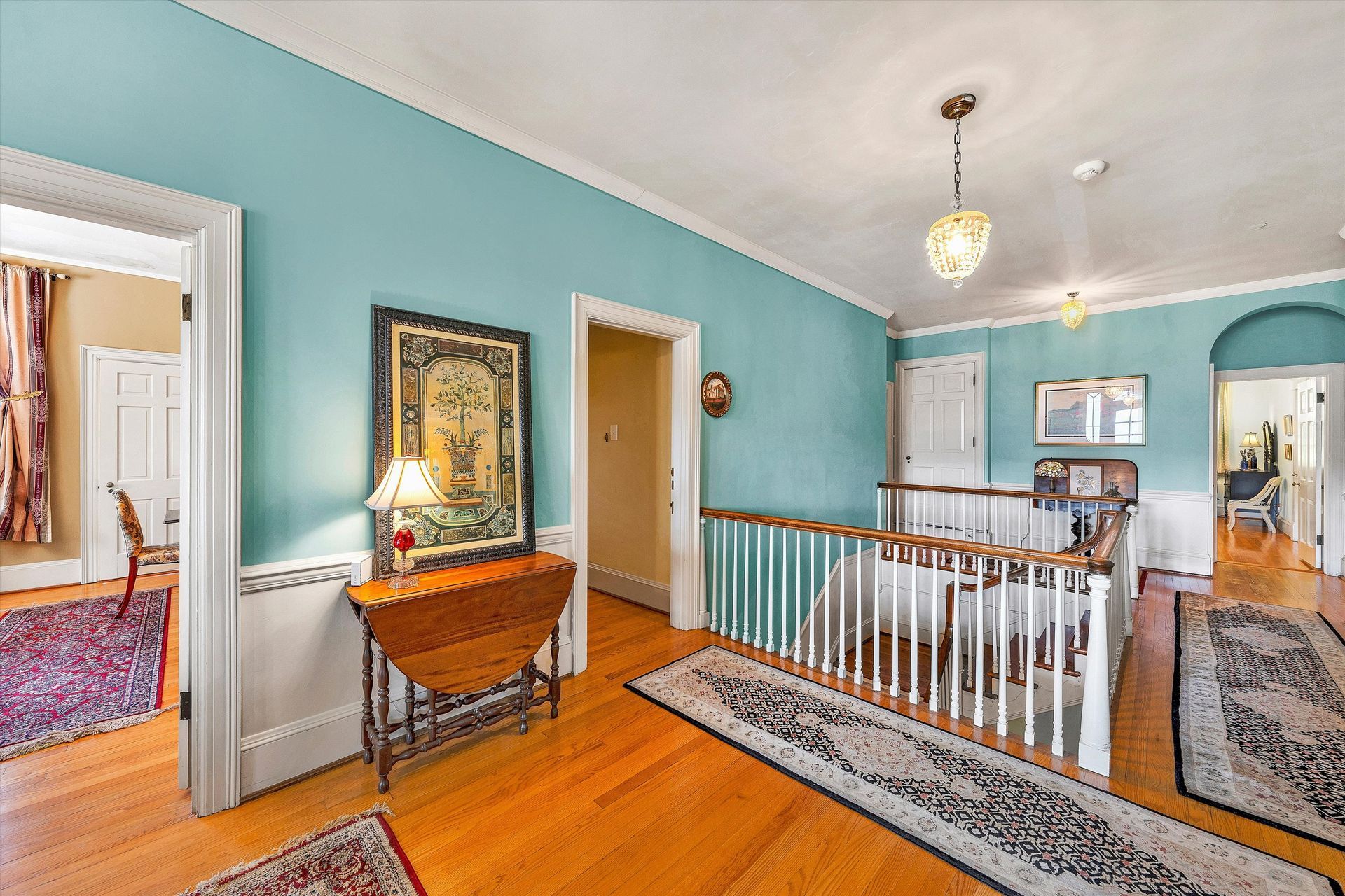 Bright foyer with turquoise walls, hardwood floors, staircase railing, and a small console table with mirror.