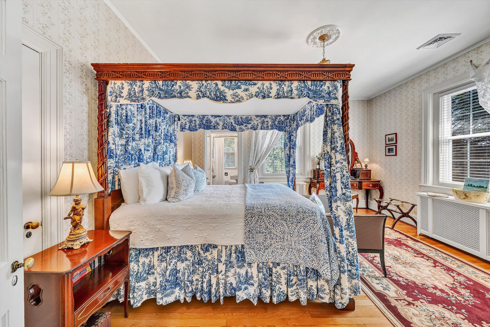 Elegant bedroom with a four-poster bed, floral curtains, and a bedside lamp by a window